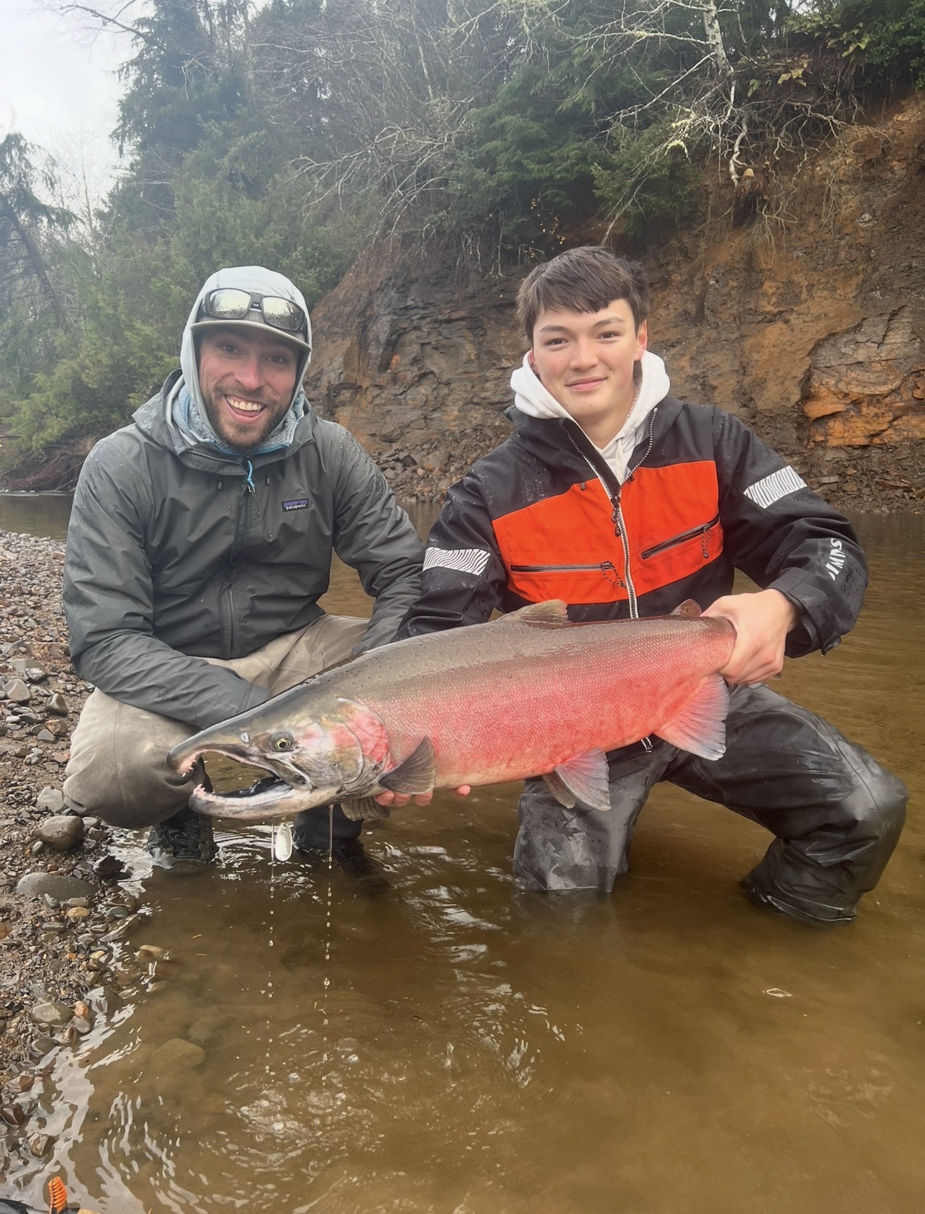 Two anglers kneeling in shallow water with a bright salmon