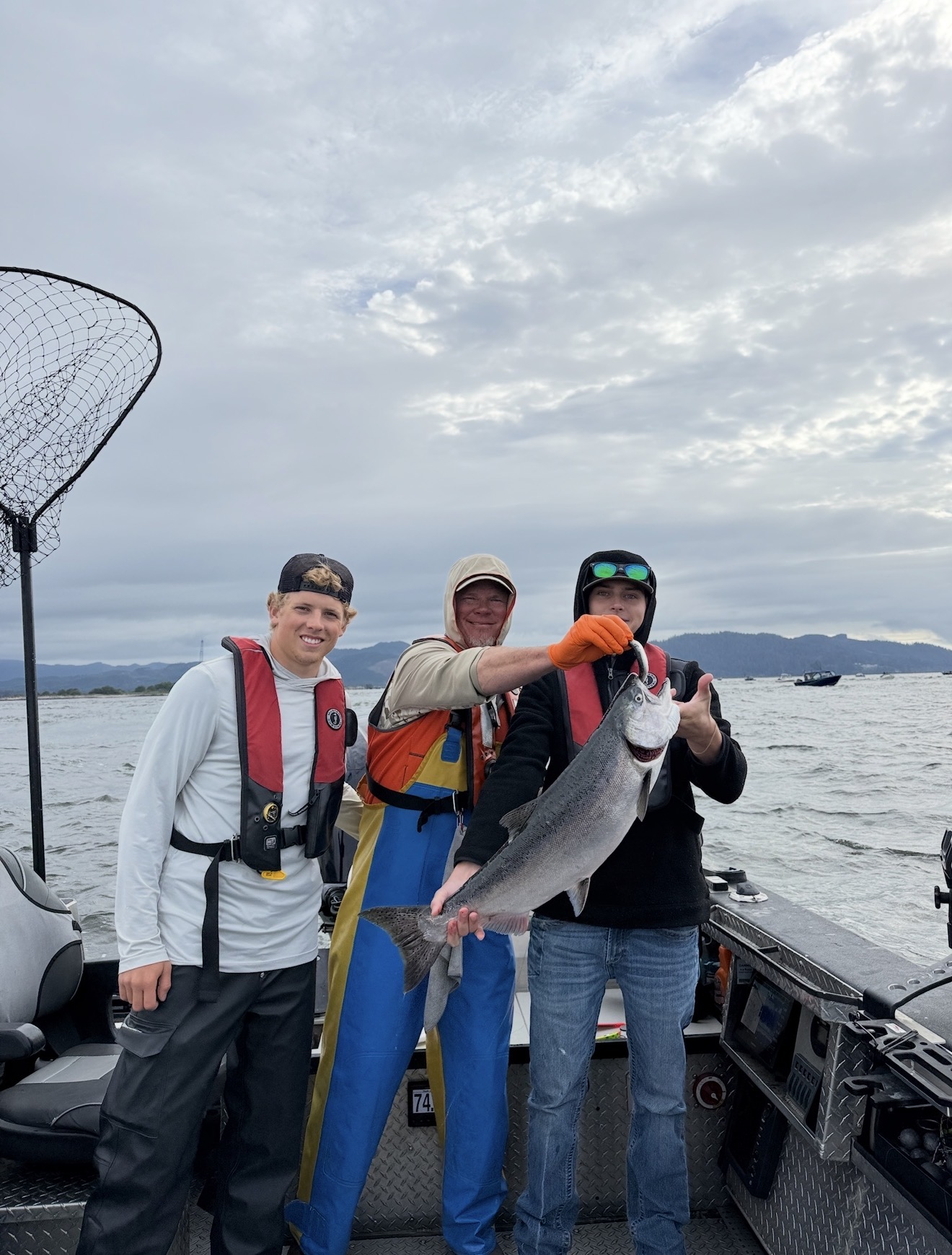 Three anglers on the boat holding a chrome Chinook salmon