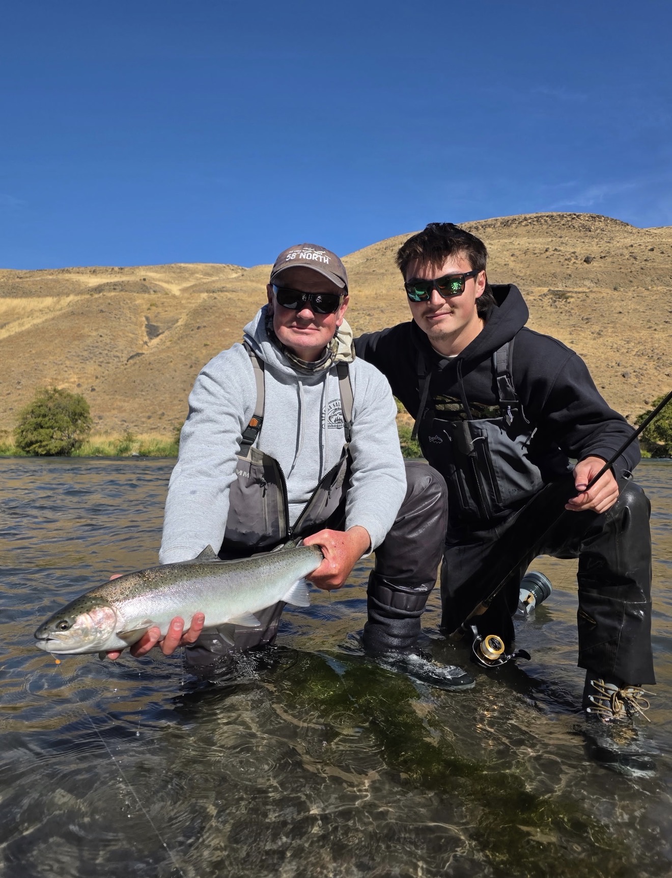 Captain Judd and client kneeling in the Deschutes River with a chrome steelhead