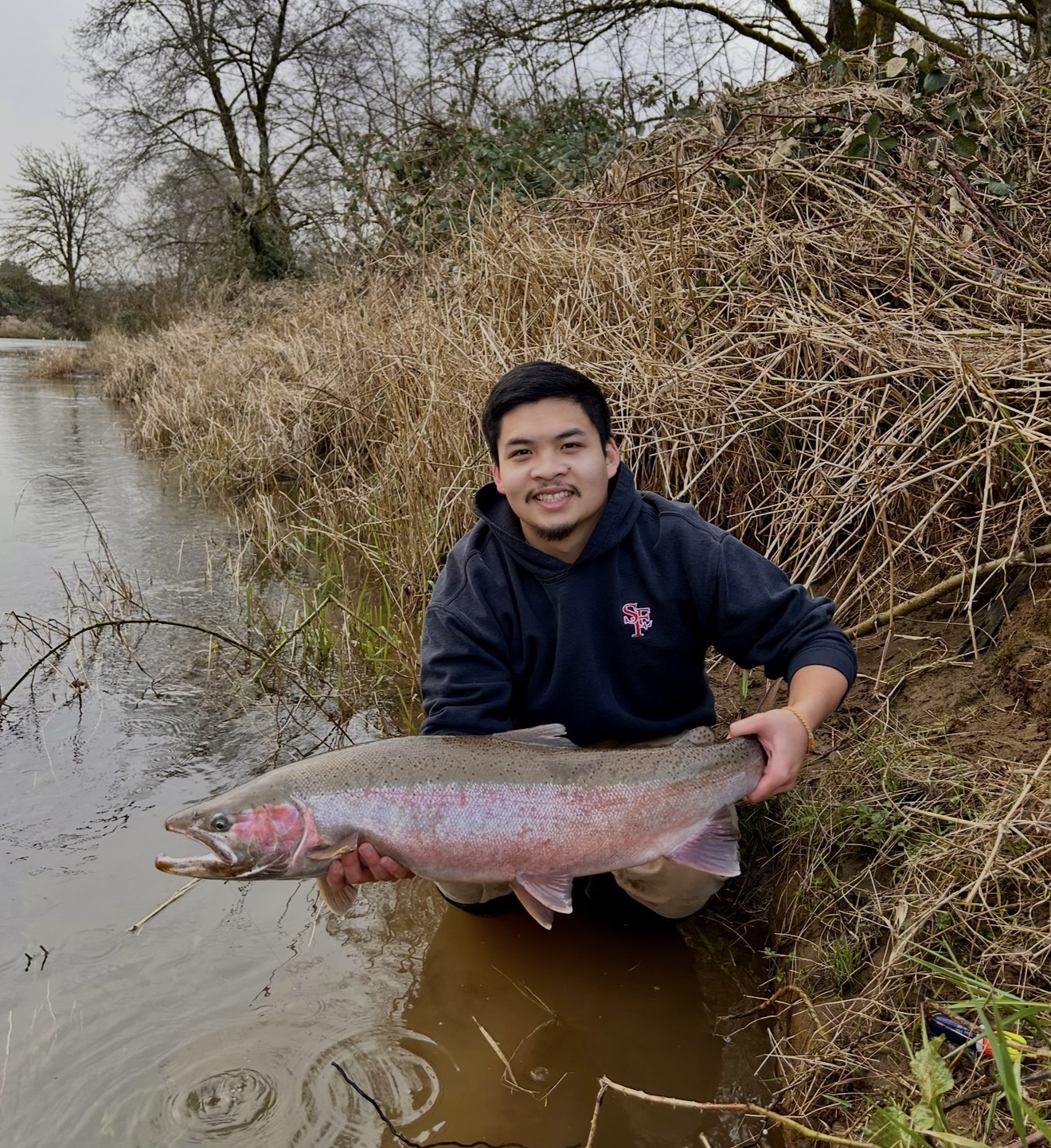 Client kneeling on the riverbank with a huge chrome steelhead