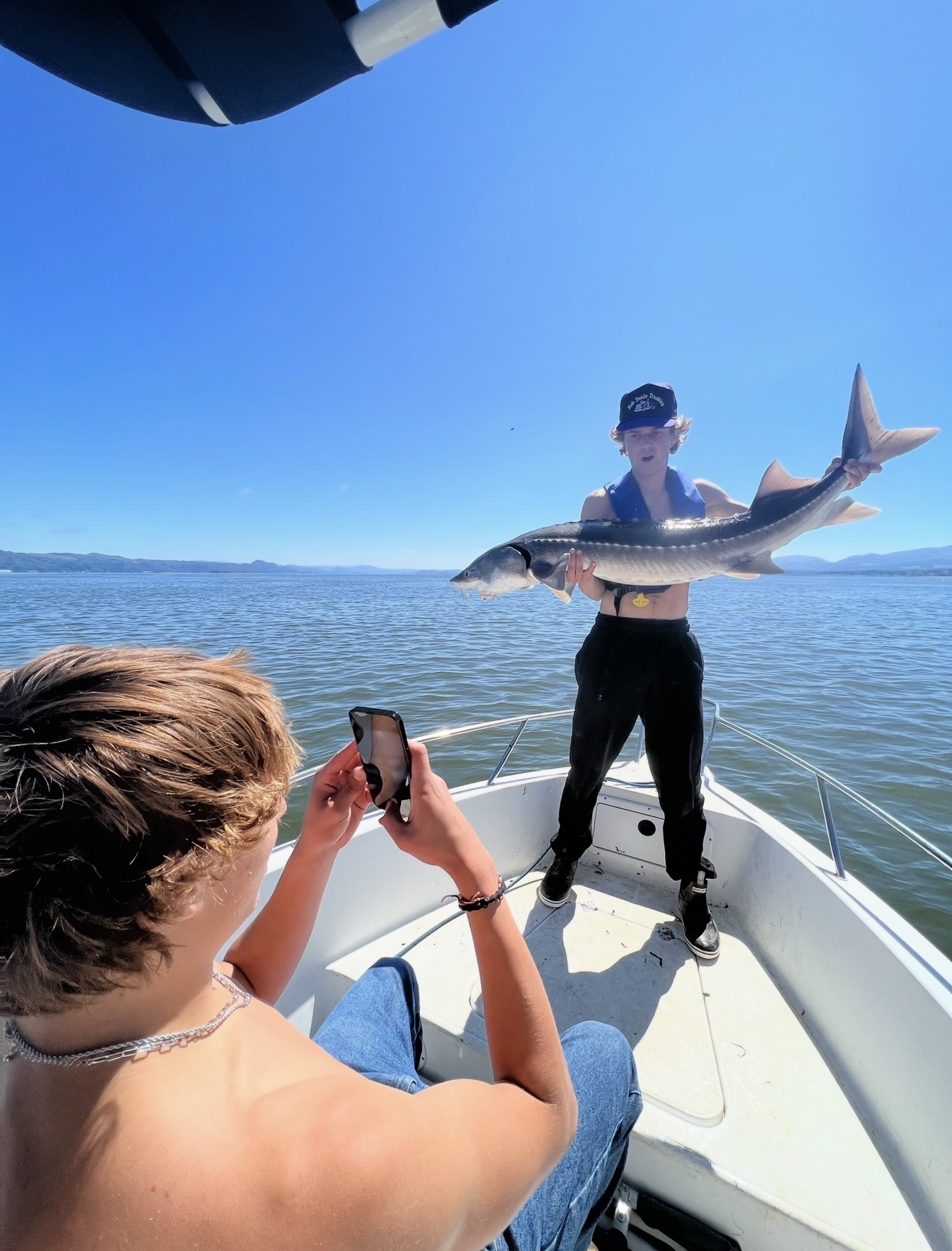 Client photographing another angler hoisting a sturgeon on a bluebird day