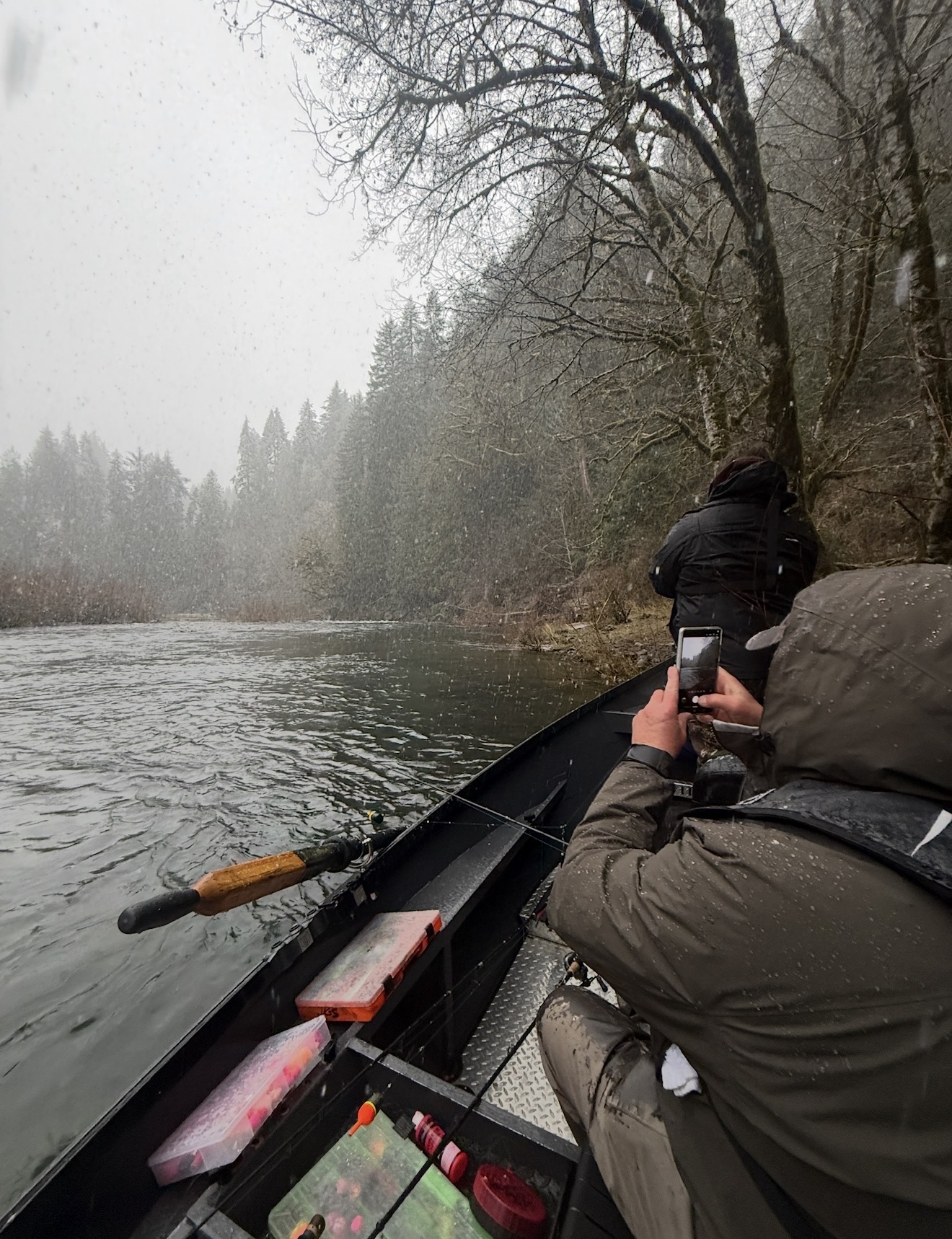 Client on a drift boat photographing the misty Oregon river in falling snow