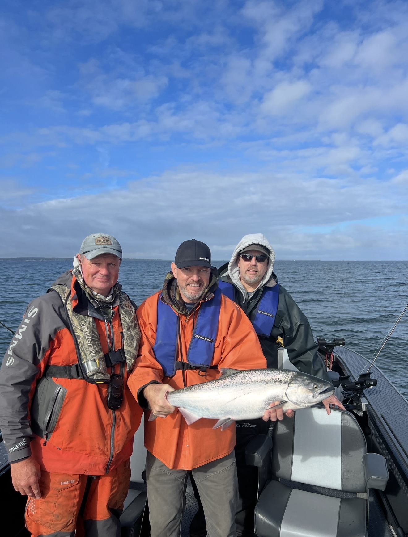 Three anglers on the ocean boat holding a bright Chinook salmon