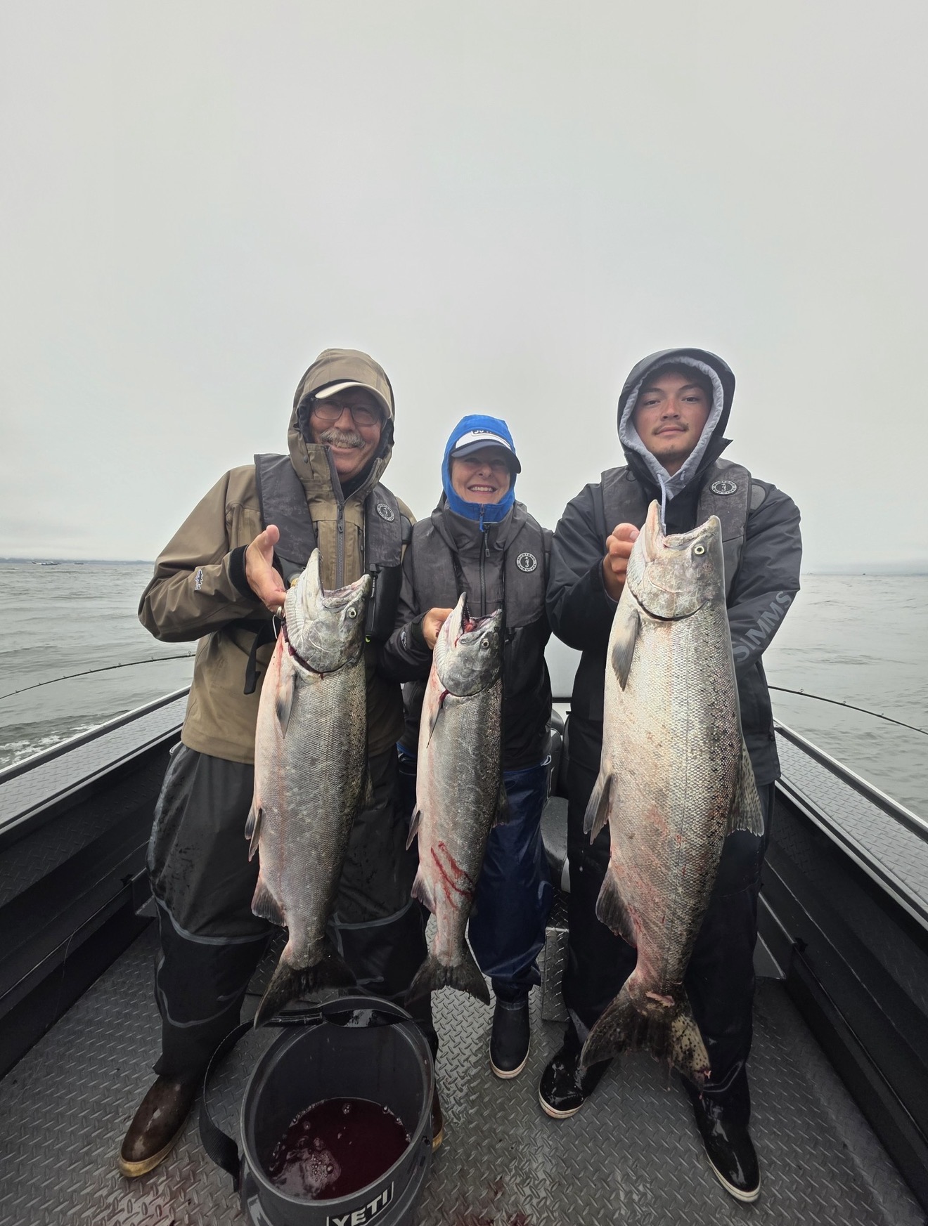 Family on the boat holding three bright Buoy 10 Chinook