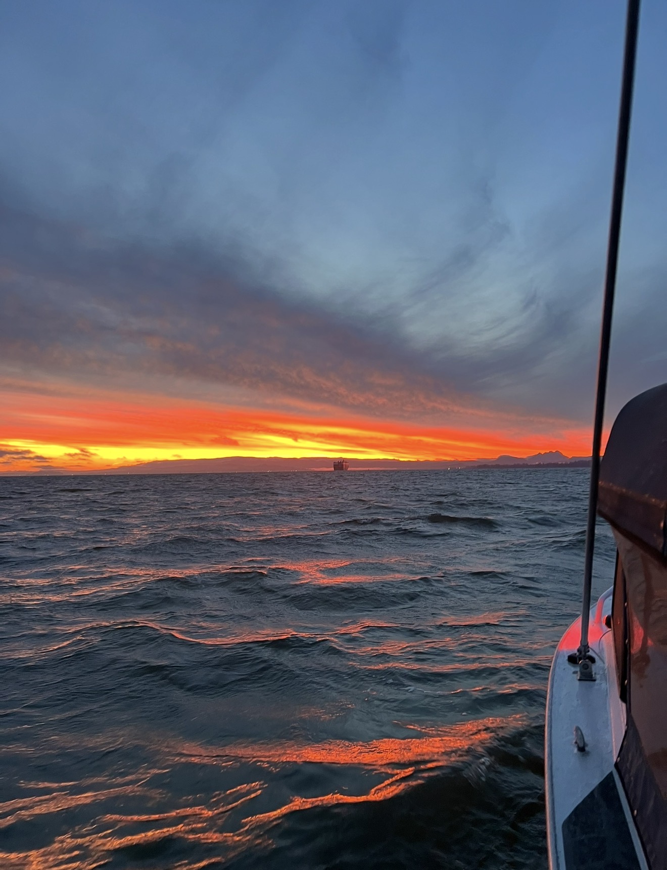 Fiery orange sunset over the Columbia River from the boat with a ship on the horizon
