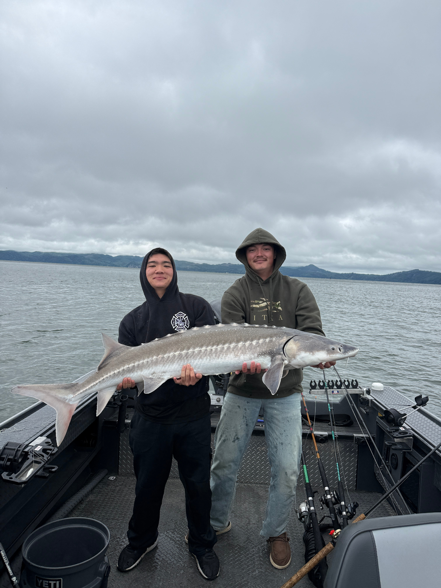 Two clients holding a huge Columbia River sturgeon on a cloudy day