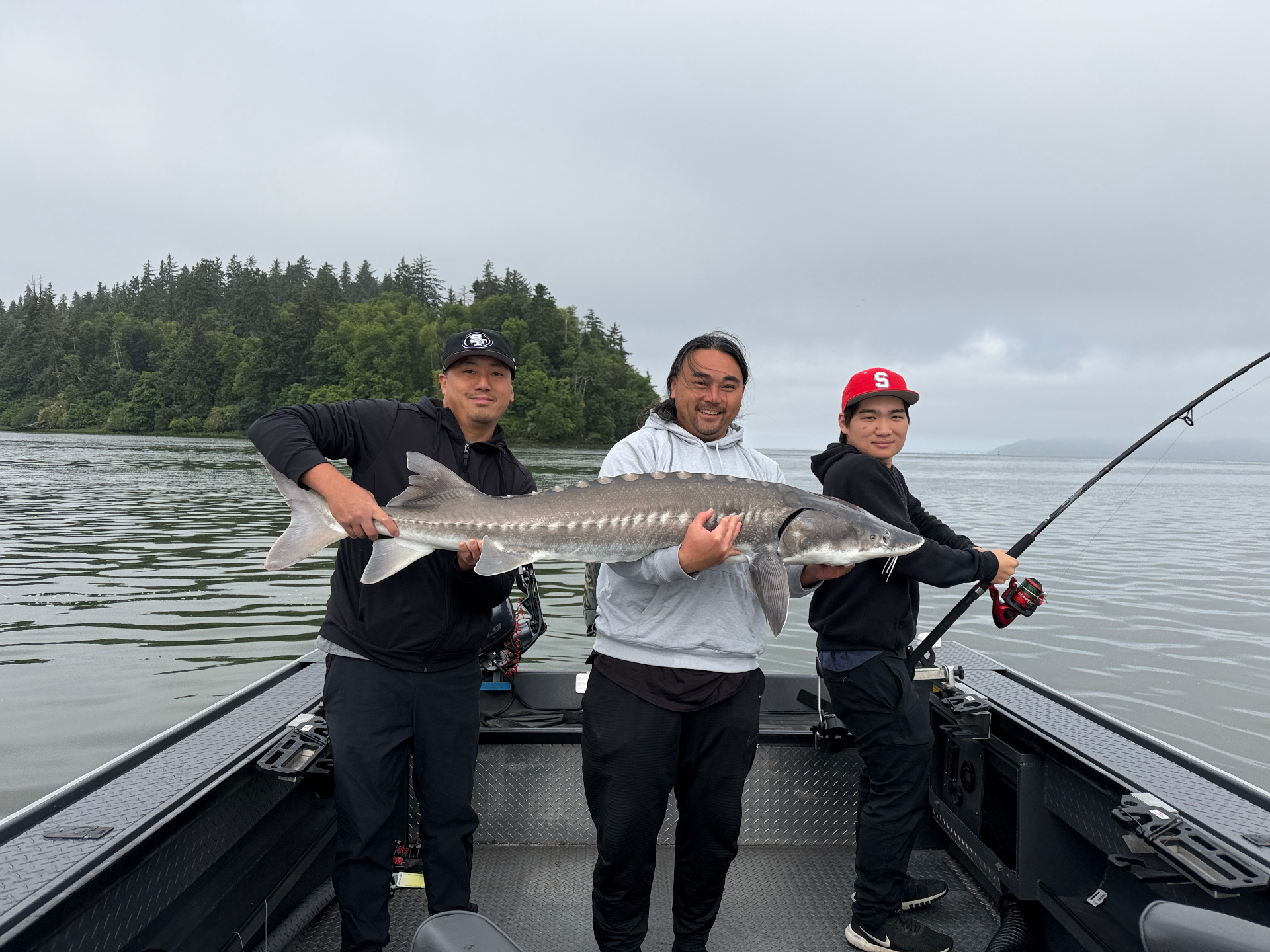Three anglers on the boat holding a large Columbia River sturgeon