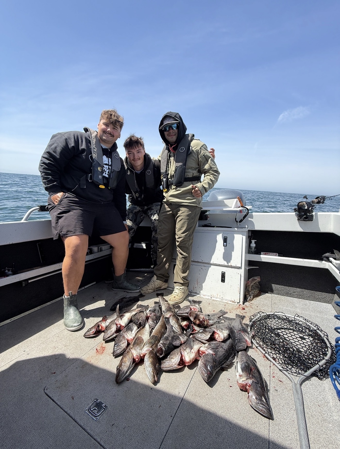 Three anglers on the ocean boat with a full haul of lingcod and rockfish on deck