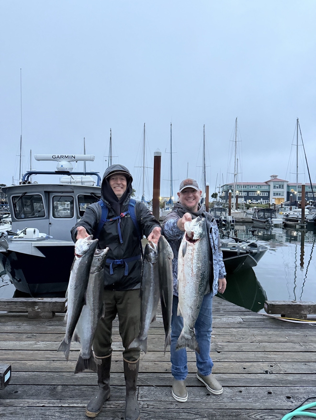Two anglers on the dock holding a mixed bag of salmon in the harbor