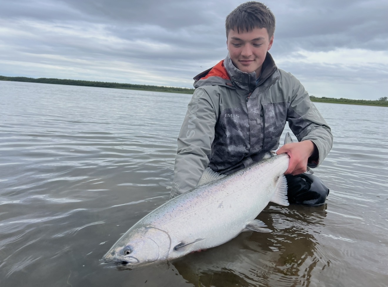 Angler kneeling in the water with a chrome bright Chinook salmon