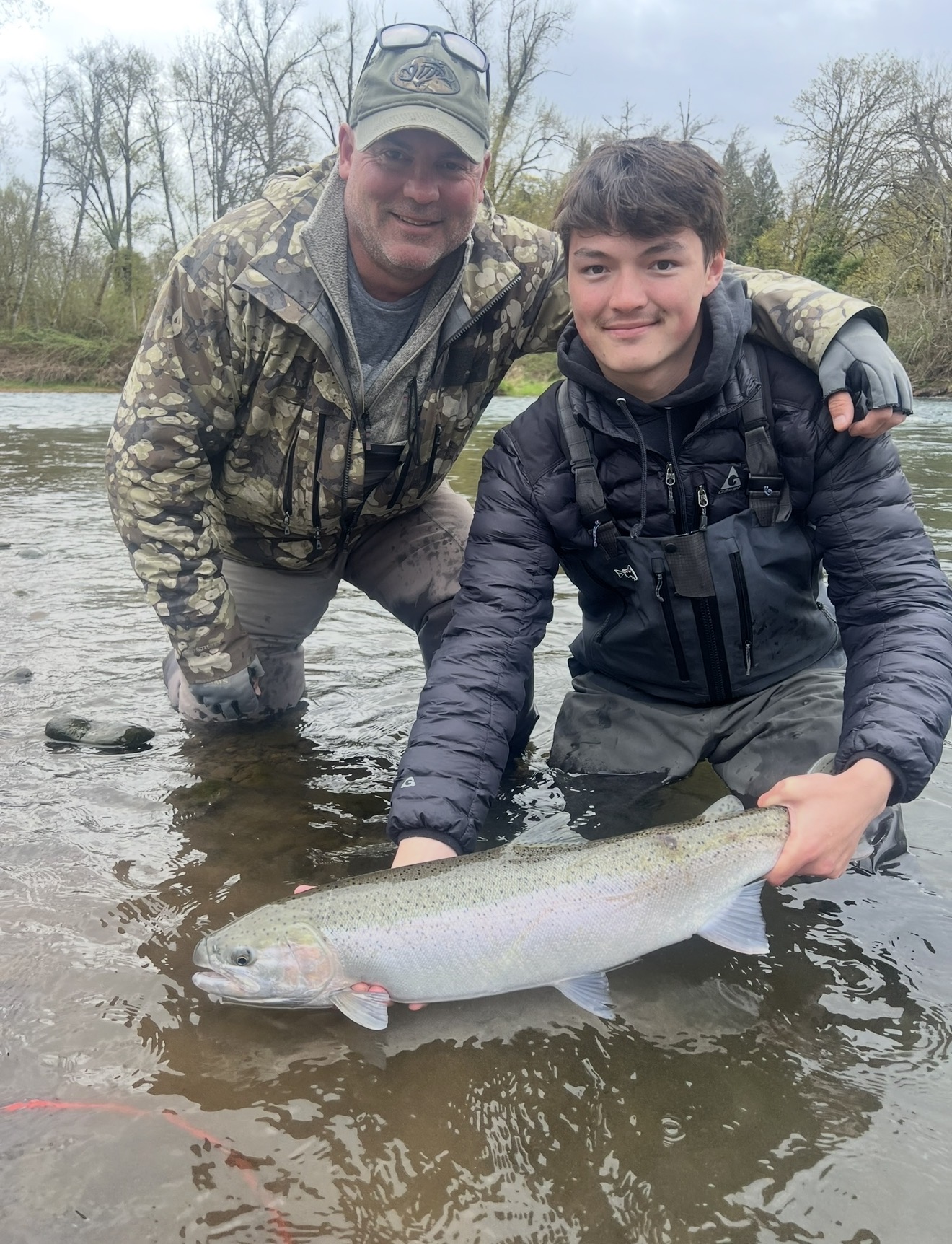 Client and guide kneeling in the river with a bright steelhead