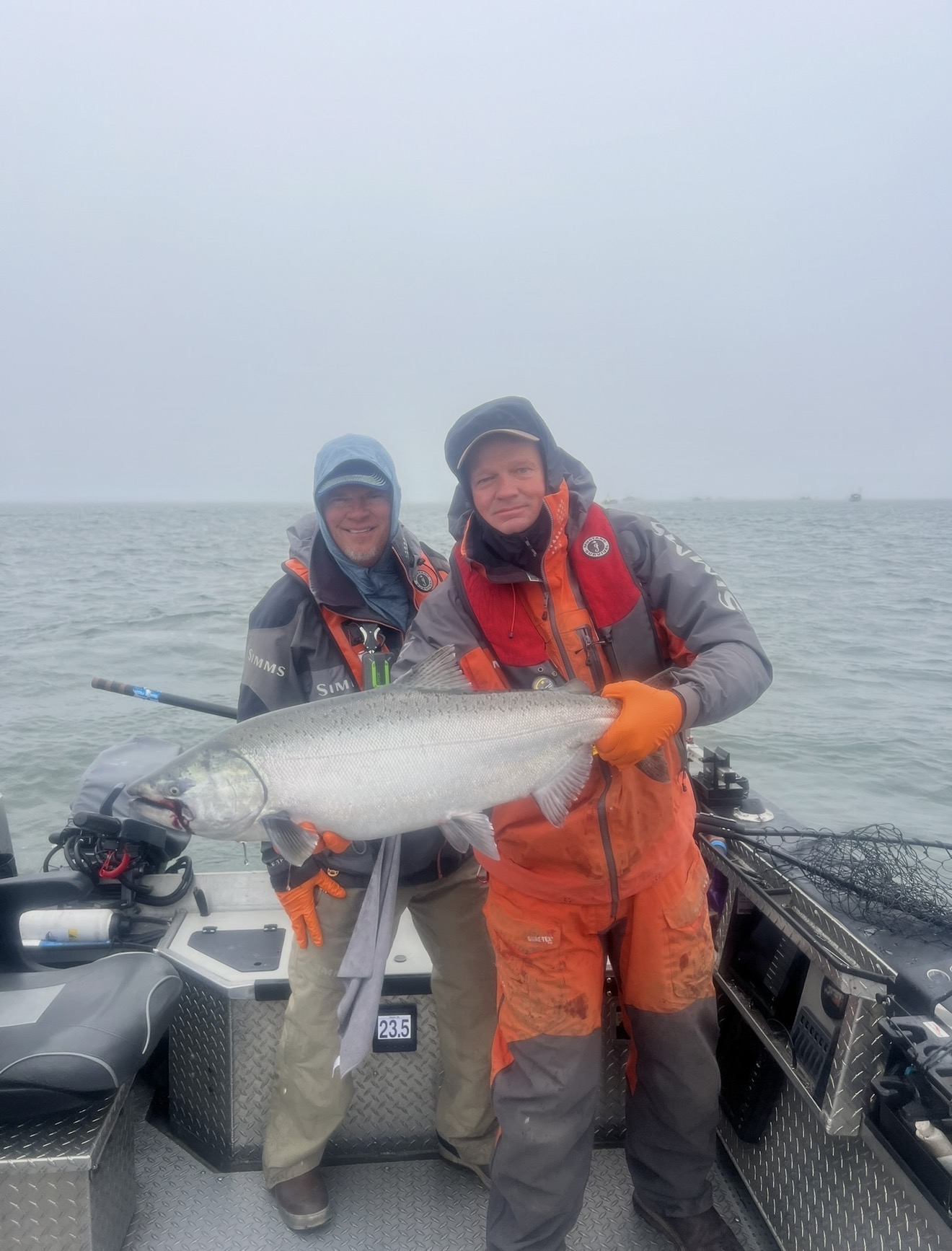 Two anglers in Simms rain gear holding a bright Buoy 10 Chinook salmon