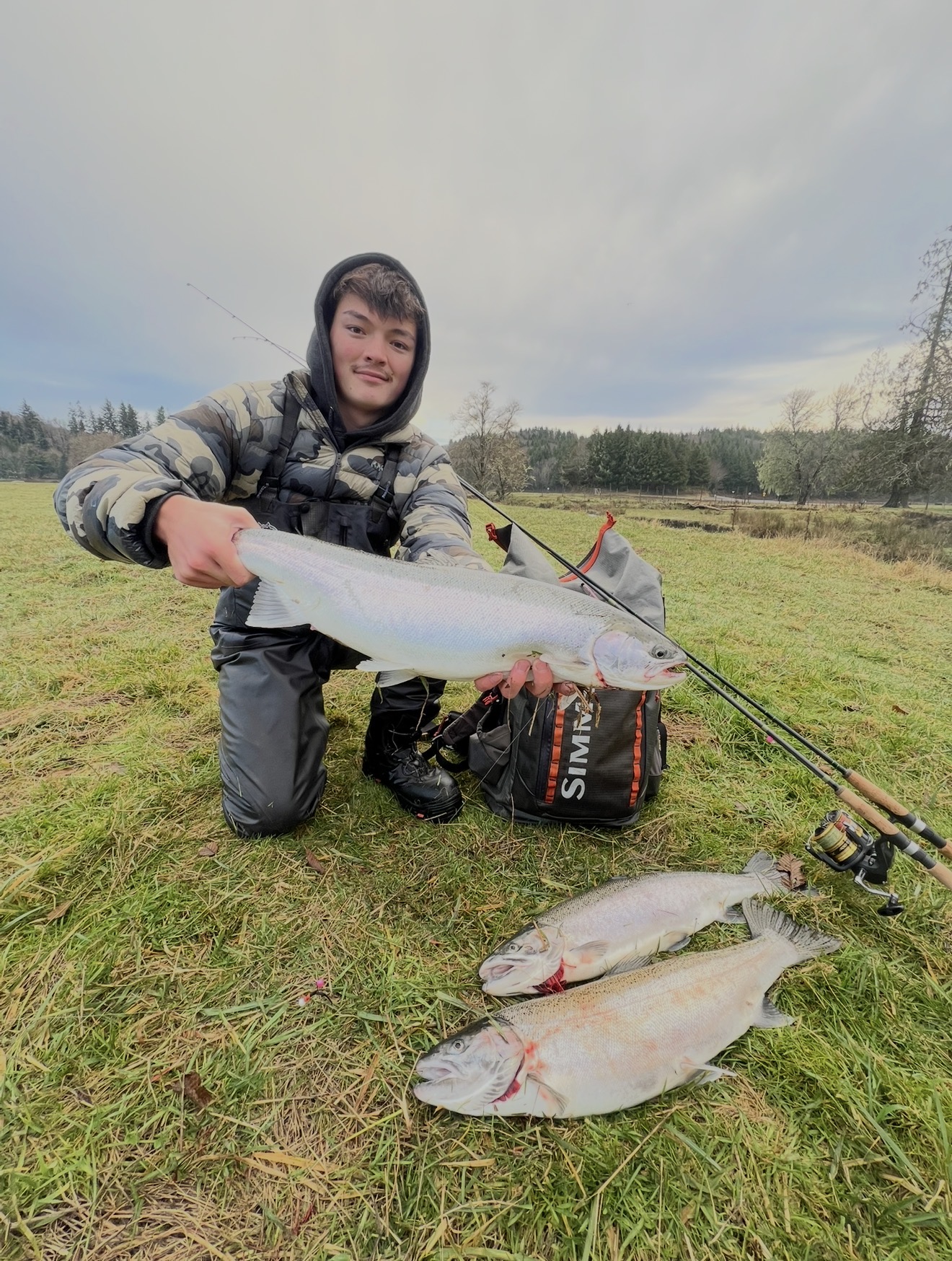 Angler kneeling in a field with a limit of bright coho salmon