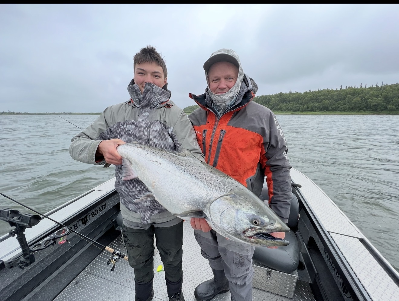 Two anglers on the boat holding a bright Chinook salmon on the river