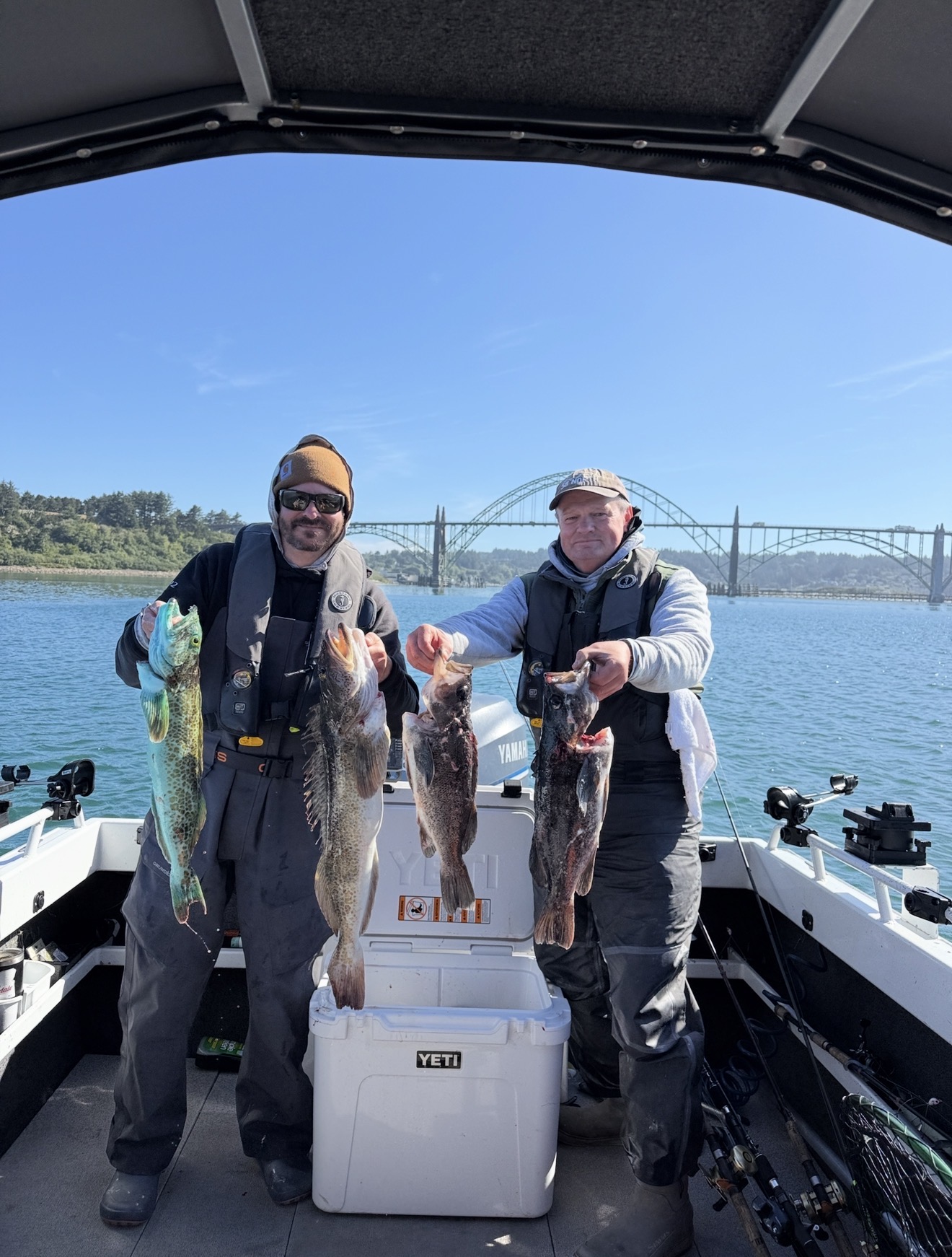 Two anglers holding lingcod and rockfish in front of the Yaquina Bay Bridge in Newport