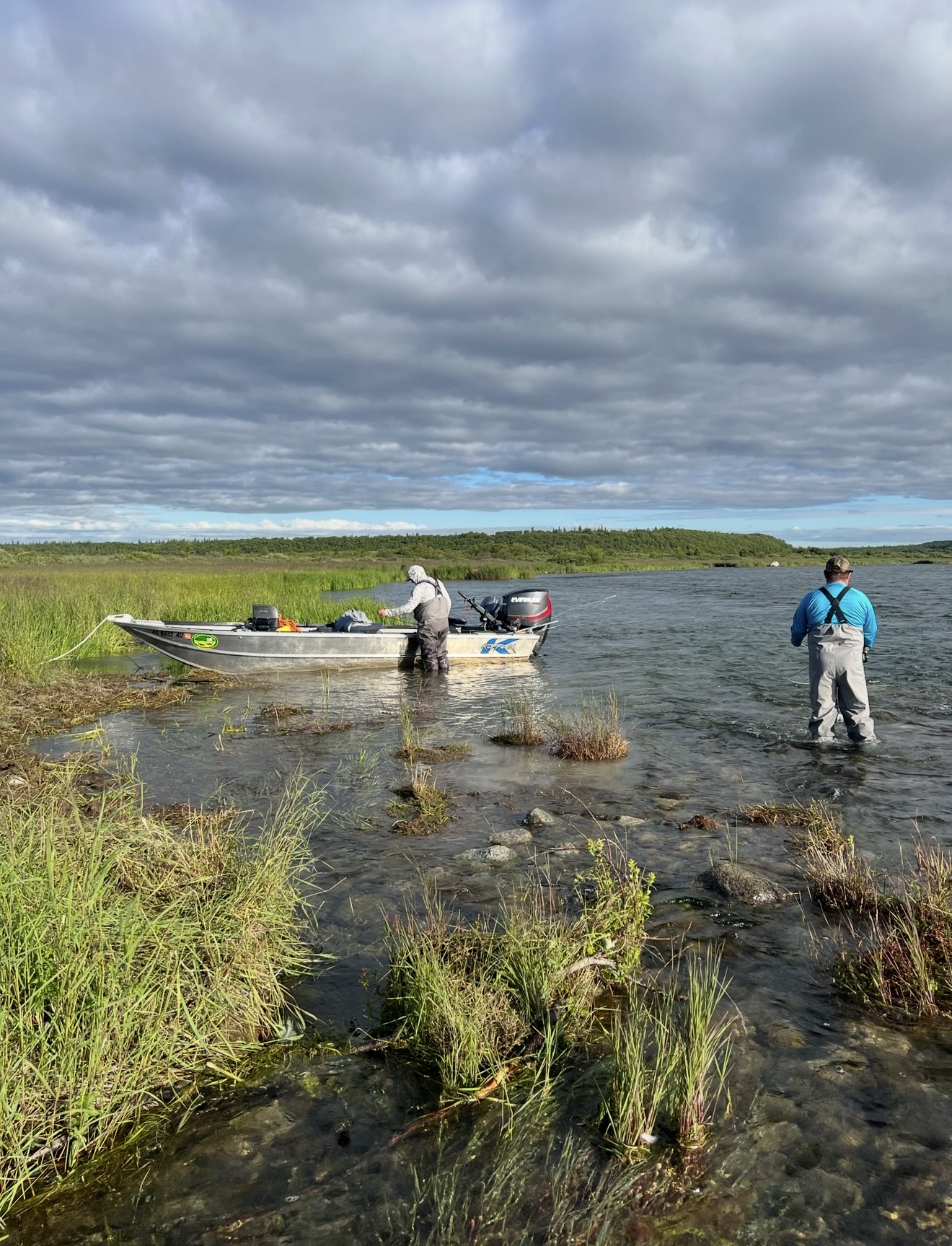 Two anglers wading an Alaska river with the aluminum boat beached in the grass